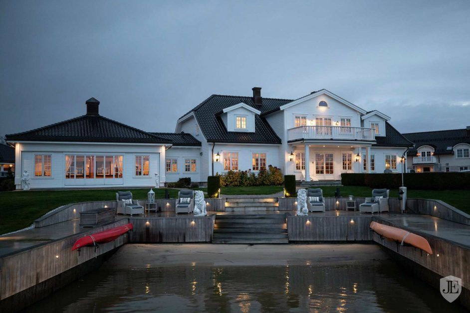 Luxury white Norwegian waterfront villa illuminated at dusk with private dock